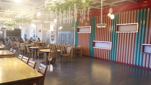 A restaurant interior with wooden tables and chairs, striped walls, hanging plants, and pendant lighting. - Singapore City Hotel (Batu Bara)