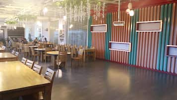 A restaurant interior with wooden tables and chairs, striped walls, hanging plants, and pendant lighting.