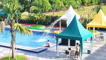 A swimming pool with a water fountain, surrounded by palm trees and covered seating areas.
