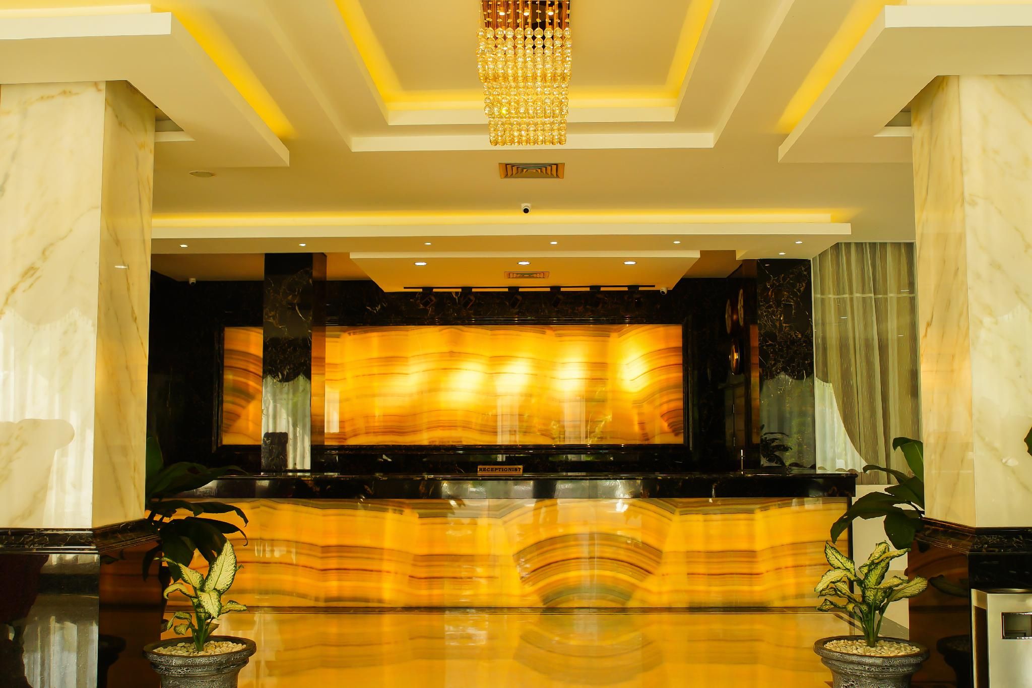 A reception area with a marble reception desk, a chandelier, and potted plants.