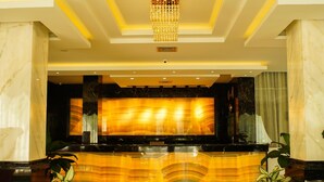 A reception area with a marble reception desk, a chandelier, and potted plants. - Singapore City Hotel (Batu Bara)