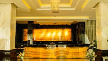 A reception area with a marble reception desk, a chandelier, and potted plants.