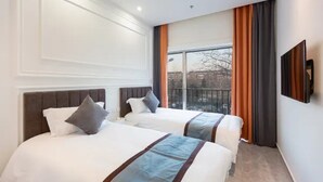 Quarto de hotel com duas camas, uma janela grande e televisão de tela plana.