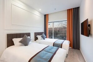 Habitación de hotel con dos camas, un ventanal grande y un televisor de pantalla plana.