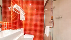 Casa de banho com parede revestida a azulejos vermelhos, banheira branca, sanita branca e cabine de duche com divisória de vidro.