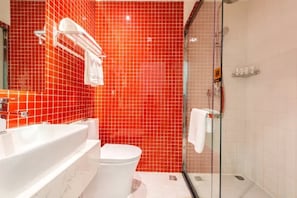 Un baño con pared de azulejos rojos, una bañera blanca, un inodoro blanco y una zona de ducha con mampara de vidrio.