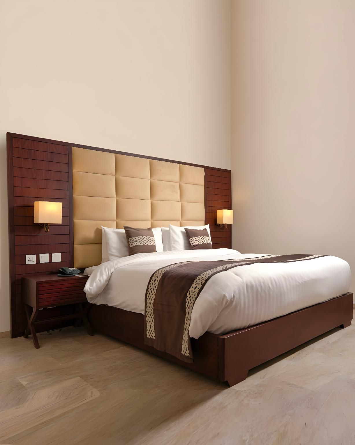 Una habitación de hotel con una cama grande, cabecero de madera, lámparas de noche y una mesita de noche.