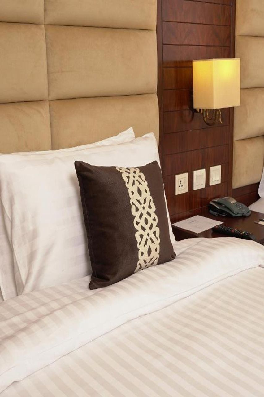 Habitación de hotel con una cama grande, cabecera con lámpara y mesita de noche con control remoto.