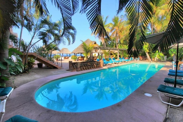 A swimming pool with lounge chairs, palm trees, and a thatched-roof structure. - Hotel Santa Fe Puerto Escondido (Santa María Colotepec)