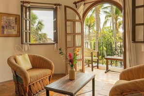 A room with a wicker sofa, a small wooden table, and a view of palm trees through a large arched window. - Hotel Santa Fe Puerto Escondido (Santa María Colotepec)