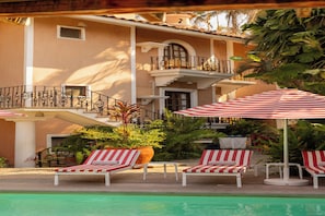 A poolside area with lounge chairs and umbrellas, a staircase, and a building with a balcony. - Hotel Santa Fe Puerto Escondido (Santa María Colotepec)