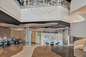 Een ruime lobby met een modern ontwerp, met een gebogen receptiebalie, een zithoek en een groot muurdecoratie.