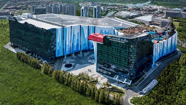 Un edificio moderno con fachada de vidrio y un llamativo diseño azul y blanco, rodeado de vegetación y un río.
