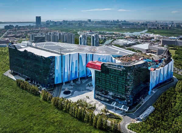 Een modern gebouw met een glazen gevel en een opvallend blauw-wit ontwerp, omgeven door groen en een rivier.