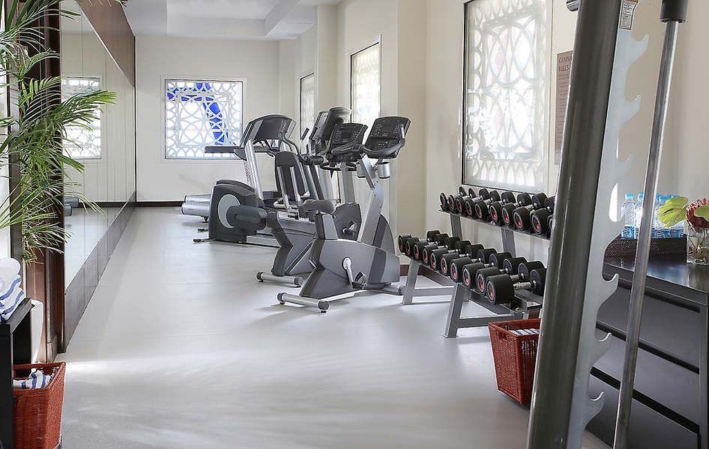 A gym with cardio machines, dumbbells, and a mirrored wall.