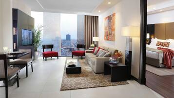 A modern hotel room with a city view, a dining area, and a living space with a sofa and chairs.