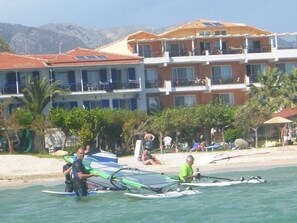 A coastal hotel with multiple balconies, a beach in the background, and people engaging in water activities. - Nefeli Wind Club (Lefkada)