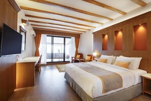 A hotel room with a large bed, a desk, a TV, and a sliding glass door leading to a balcony. - Club Himalaya by ACE Hotels (Baluwapati Deupur)