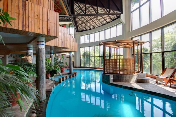 An indoor swimming pool with wooden beams, large windows, and potted plants. - Club Himalaya by ACE Hotels (Baluwapati Deupur)