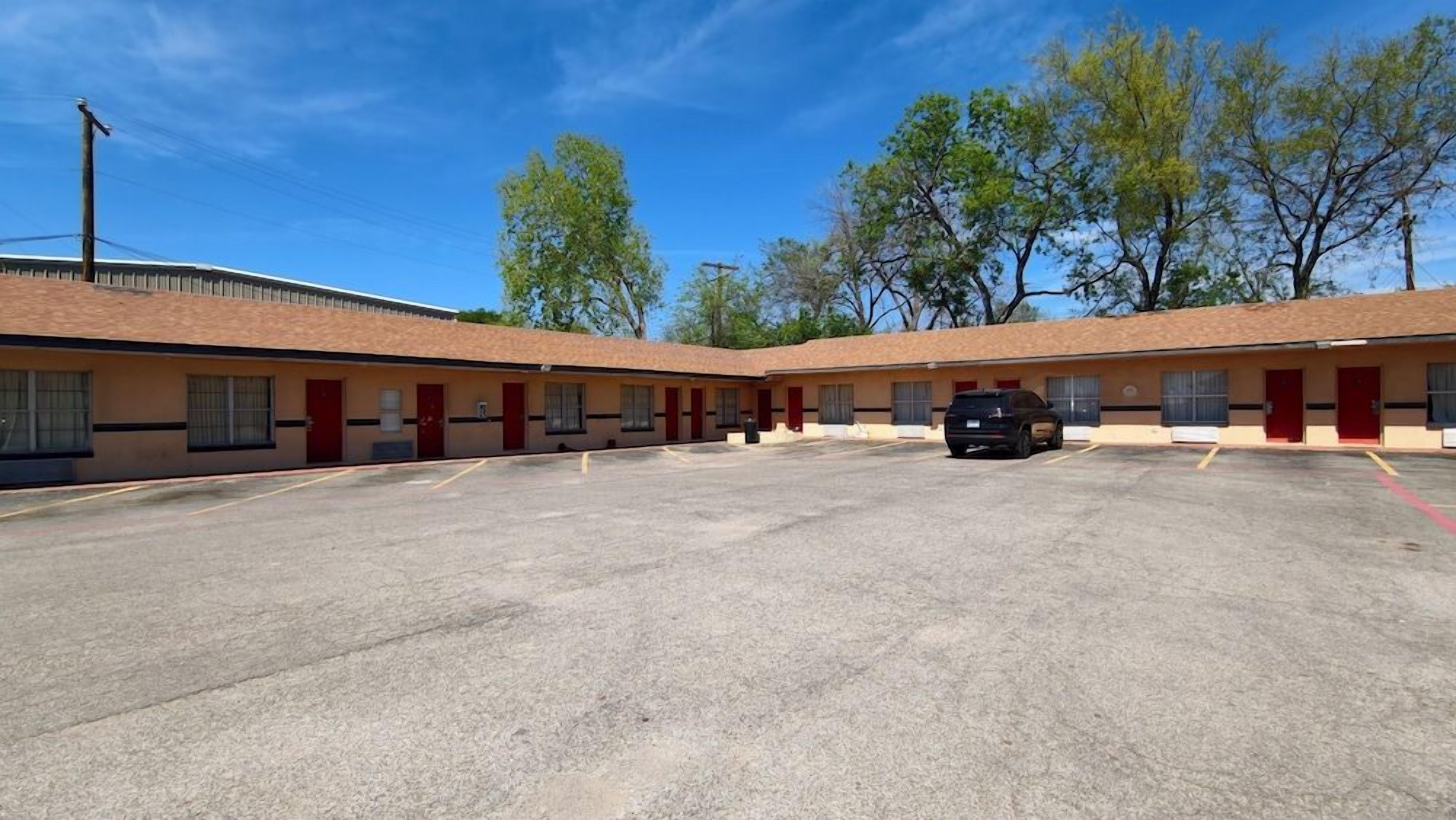 A motel with a row of rooms, a parking lot, and trees in the background.