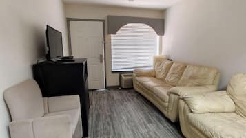 A room with a beige leather sofa, a black entertainment unit, and a white armchair.