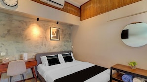 A hotel room with a bed, desk, chair, and a small shelf with towels. - Collection O Near Sanur Beach Formerly Sutji Living (Denpasar)