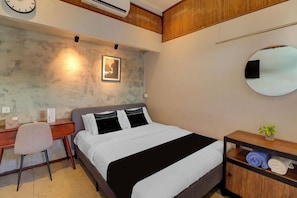 Ein Hotelzimmer mit Bett, Schreibtisch, Stuhl und einem kleinen Regal mit Handtüchern.