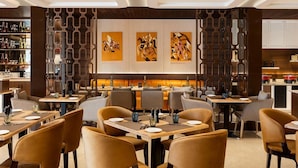 Un restaurante con una decoración moderna, que presenta una zona de bar con una variedad de botellas, un área de comedor con mesas y sillas, y arte abstracto en las paredes.