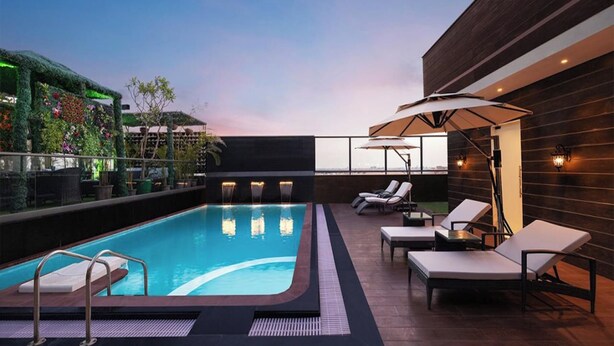 Un área de piscina en la azotea con vistas despejadas del horizonte de la ciudad, sillas de descanso y una pared decorativa con plantas.