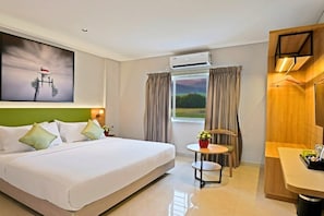 Habitación de hotel con cama, una pequeña mesa con una planta, un equipo de aire acondicionado, una ventana con cortinas y un armario de madera.