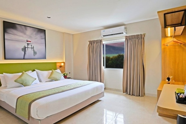 Una habitación de hotel con cama, escritorio, aire acondicionado y ventana con cortinas.