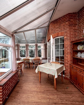 A covered patio area with brick walls, wooden tables, and chairs. - Trivelles Waterhall Country Hotel (Crawley)