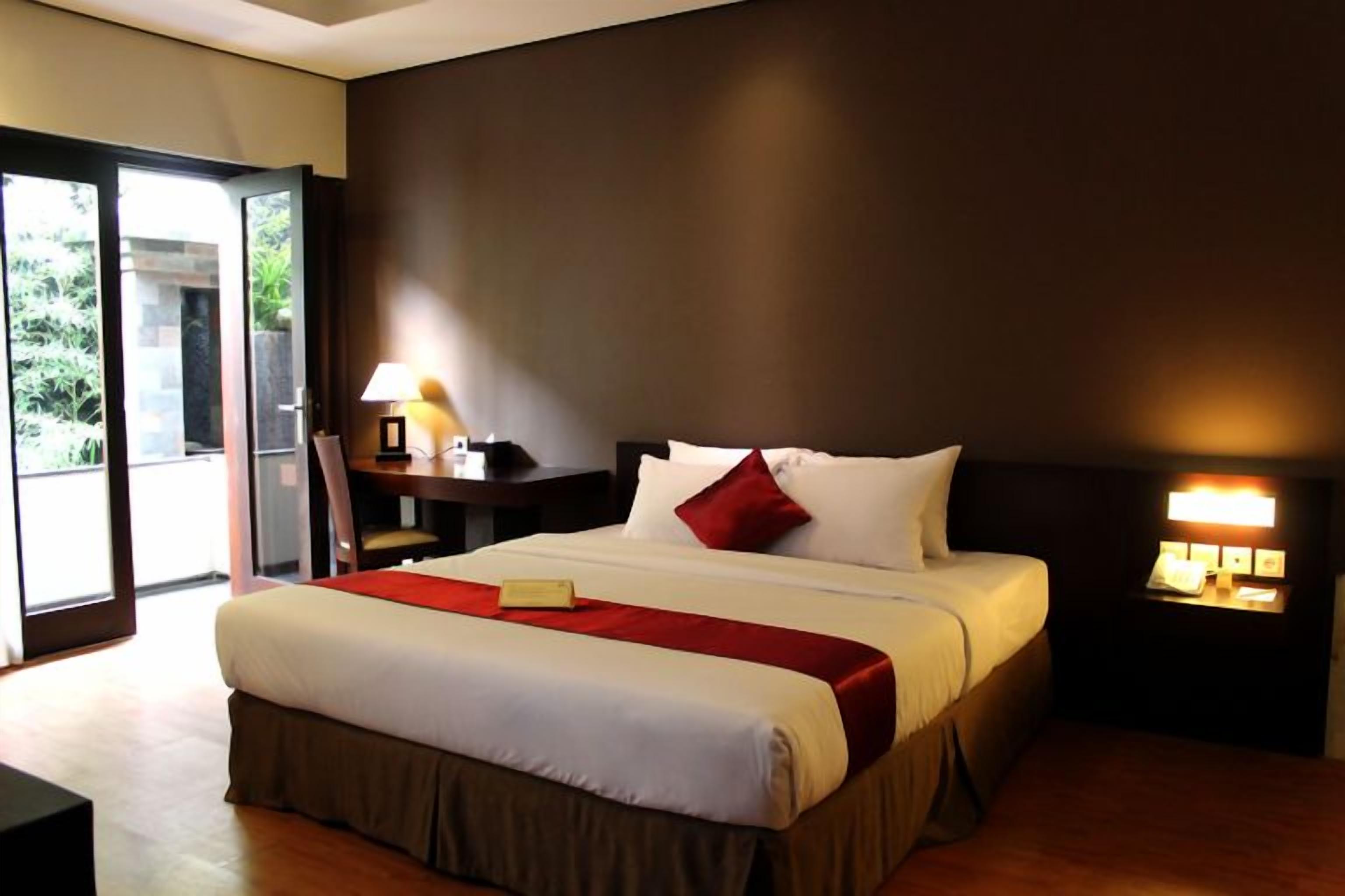 Habitación de hotel con una cama grande, un escritorio, una silla y una mesita de noche con lámpara.