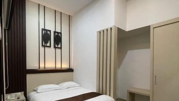 A modern bedroom with a bed, bedside table, wardrobe, and a bench. - Dawala Hotel (Makassar)