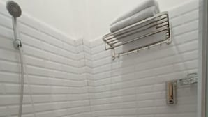 A small, white-tiled bathroom with a toilet, a shower, and a towel rack. - Dawala Hotel (Makassar)