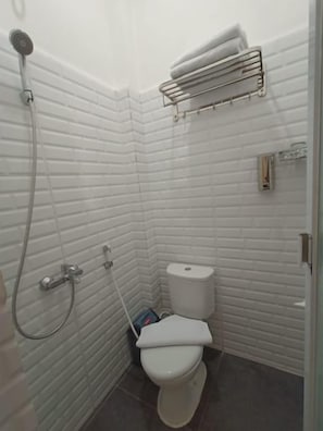 A small, white-tiled bathroom with a toilet, a shower, and a towel rack. - Dawala Hotel (Makassar)