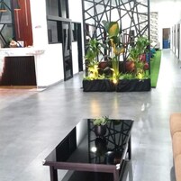 Una zona de recepción con mostrador, una mesa de vidrio con planta y un área de descanso verde.