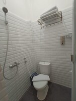 Un baño pequeño con azulejos blancos, que incluye una ducha, inodoro y perchero.