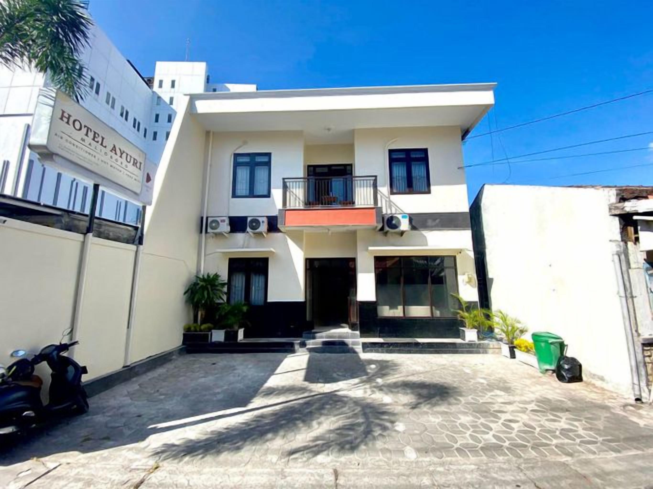 Hotel de dos pisos con fachada plana, balcón en el nivel superior y entrada protegida por una reja.