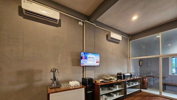 A room with a wooden floor, a white radiator, a coffee machine, a television mounted on the wall, and a window with a view. - Nusa Living Hotel Kediri (Kediri)