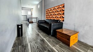 A modern interior with a wooden floor, a black leather sofa, a wooden chest of drawers, and a wall-mounted light fixture. - Nusa Living Hotel Kediri (Kediri)