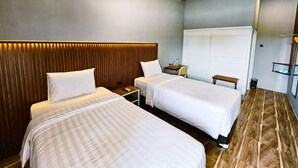 A hotel room with two beds, a wardrobe, a desk, and a chair. - Nusa Living Hotel Kediri (Kediri)