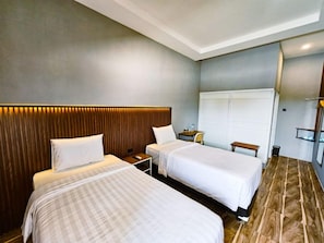 A hotel room with two beds, a wardrobe, a desk, and a chair. - Nusa Living Hotel Kediri (Kediri)