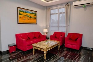 Una habitación con un sofá rojo, una mesa de centro de mármol, una lámpara y un cuadro en la pared.