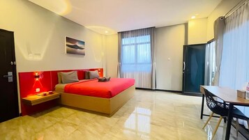 Habitación de hotel con cama, mesita de noche, lámpara y vistas al exterior.