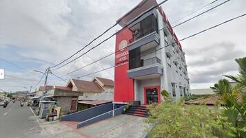 A multi-story hotel with a prominent red and white facade, a visible entrance, and a balcony on the upper floor.