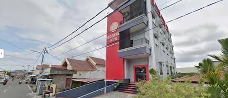 Un hotel de varios pisos con una fachada llamativa en rojo y blanco, una entrada visible y un balcón en el piso superior.