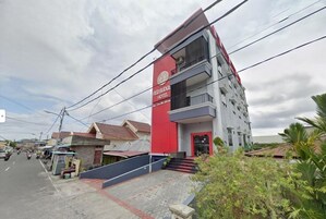 Un hotel de varios pisos con una fachada llamativa en rojo y blanco, una entrada visible y un balcón en el piso superior.