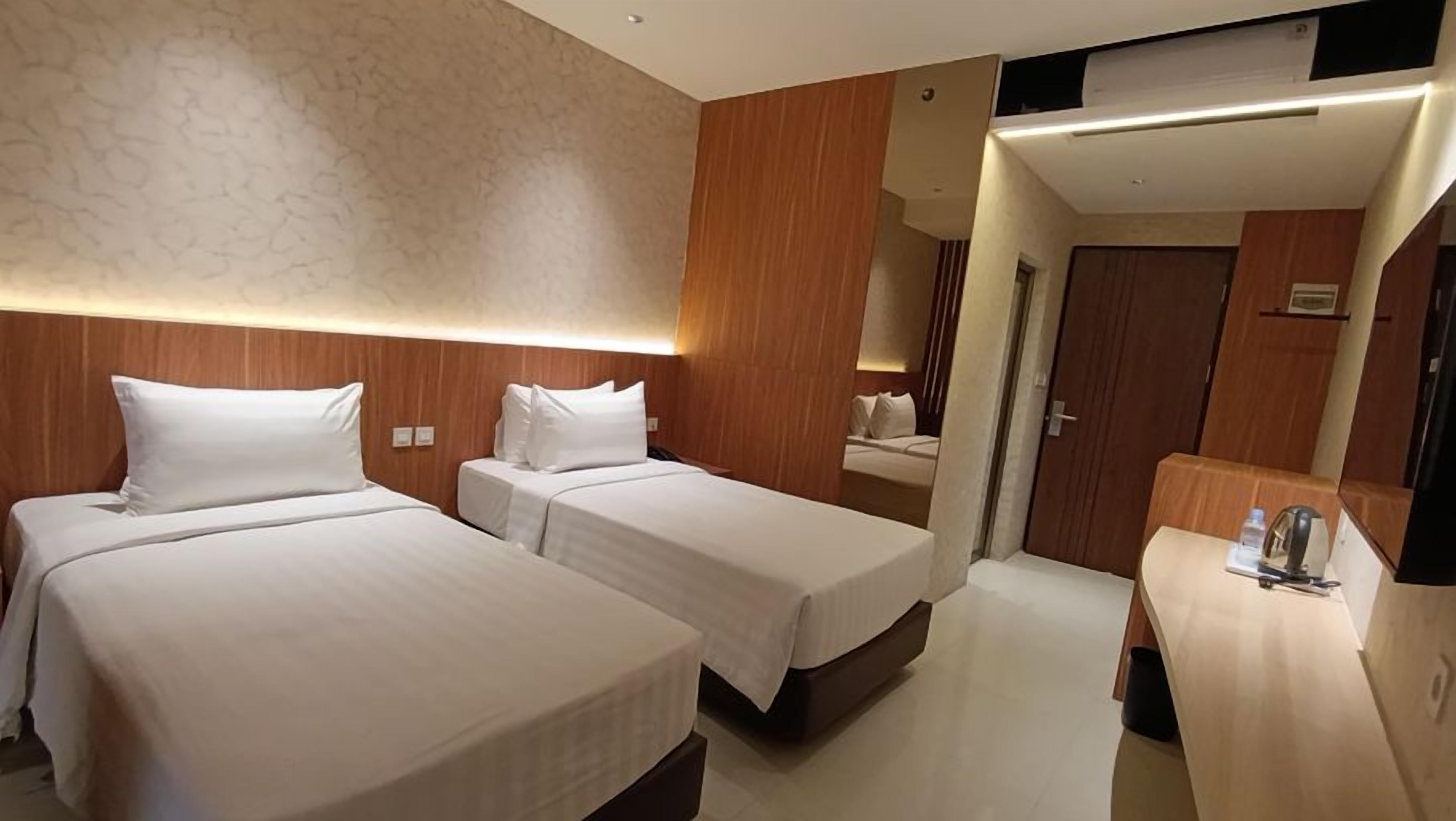 A hotel room with two single beds, a wooden headboard, a small desk with a chair, and a mirror.