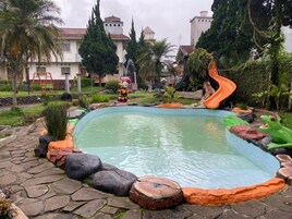 Una piscina con tobogán, rodeada de rocas y plantas.